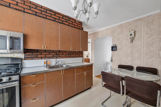 kitchen featuring wallpapered walls, a notable chandelier, appliances with stainless steel finishes, and a sink