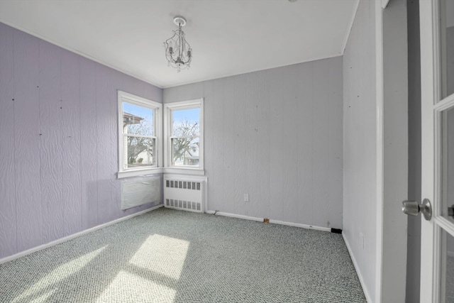 carpeted spare room featuring a chandelier, radiator, and baseboards