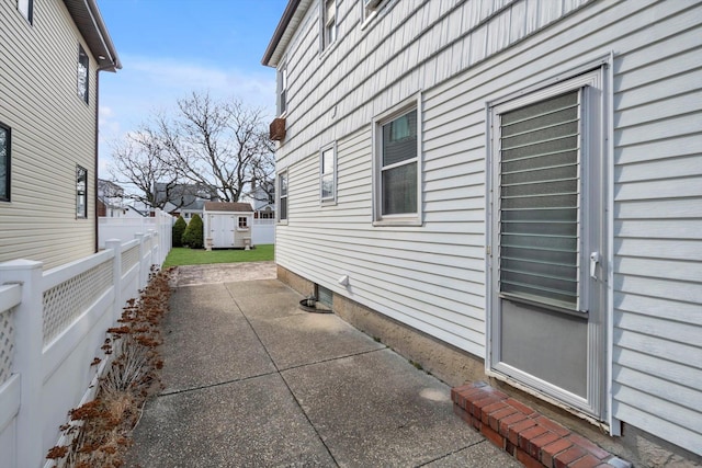 view of side of property with a patio, an outbuilding, and fence