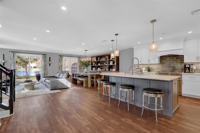 kitchen with white cabinets, dark wood-style floors, a kitchen island with sink, and a sink