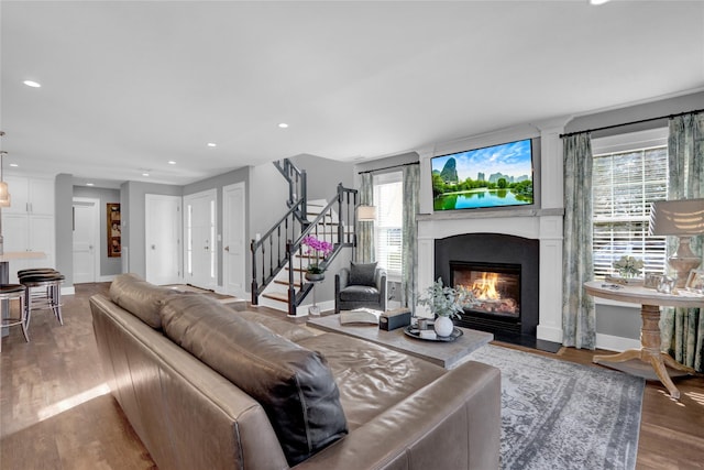 living area with a glass covered fireplace, recessed lighting, stairs, and wood finished floors