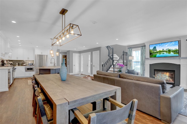 dining room featuring a glass covered fireplace, recessed lighting, light wood-type flooring, and stairs