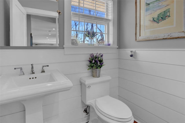 half bath featuring a sink, toilet, and wainscoting