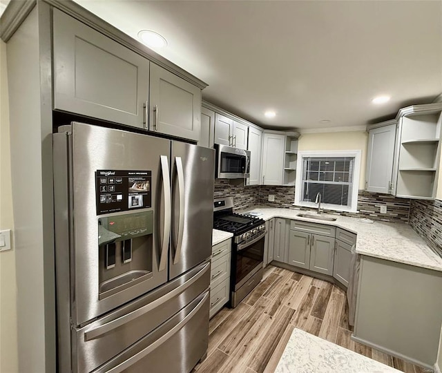 kitchen with light wood finished floors, open shelves, a sink, stainless steel appliances, and backsplash