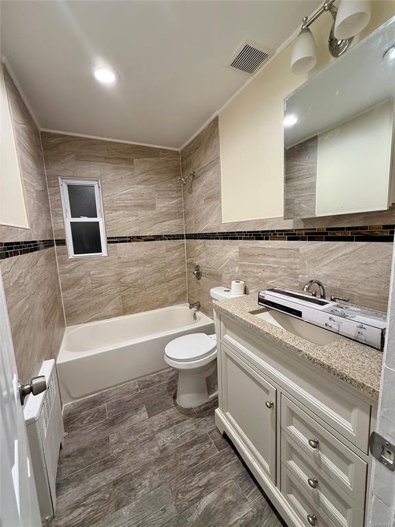 full bath featuring vanity, washtub / shower combination, visible vents, tile walls, and toilet