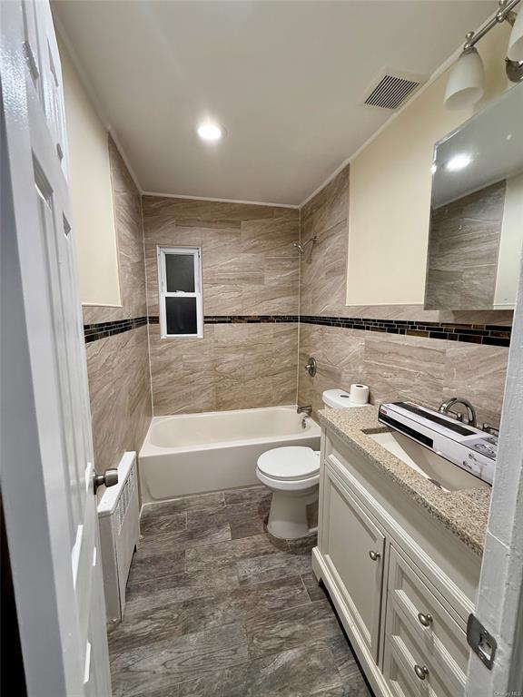 bathroom featuring visible vents, toilet, tile walls, washtub / shower combination, and vanity