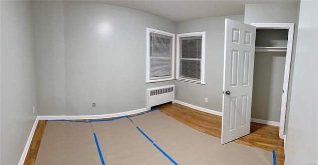 unfurnished bedroom with a closet, baseboards, wood finished floors, and radiator heating unit