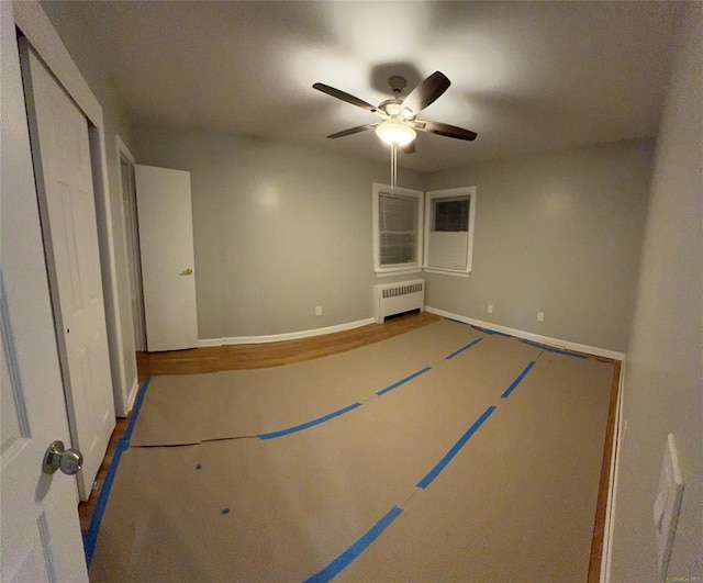 unfurnished bedroom featuring radiator, a ceiling fan, baseboards, and wood finished floors