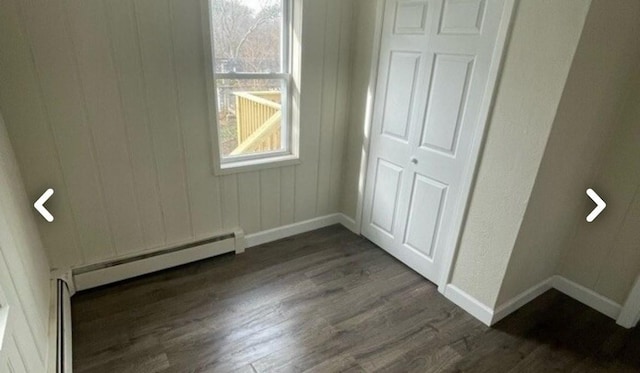 unfurnished bedroom featuring dark wood finished floors, baseboards, and baseboard heating