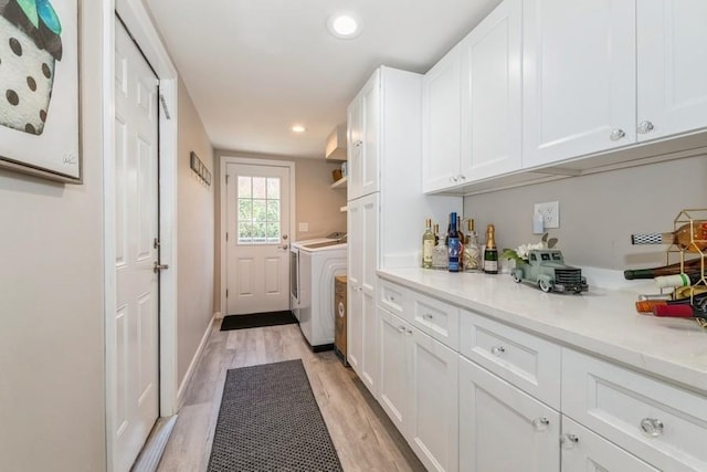 washroom featuring light wood finished floors, baseboards, washer and clothes dryer, recessed lighting, and cabinet space