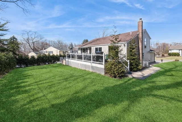 rear view of house with a deck, a yard, and a chimney