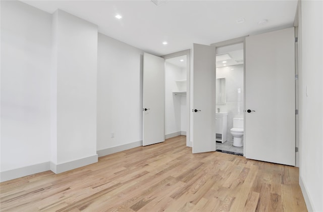 unfurnished bedroom with ensuite bath, recessed lighting, light wood finished floors, baseboards, and a spacious closet