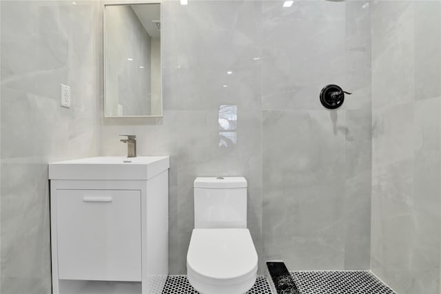 bathroom featuring tile patterned flooring, toilet, vanity, tiled shower, and tile walls