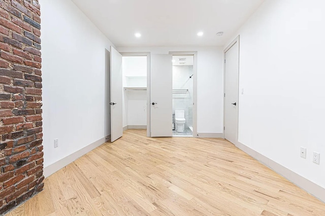 unfurnished bedroom featuring a spacious closet, baseboards, light wood-type flooring, a closet, and ensuite bath