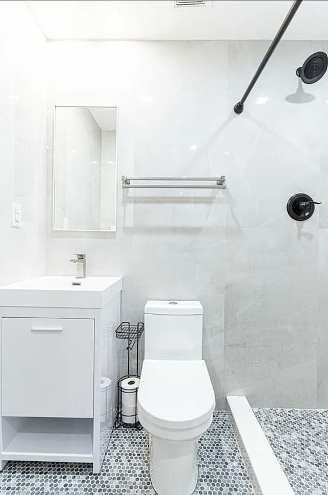 bathroom featuring tile patterned flooring, toilet, vanity, and a tile shower