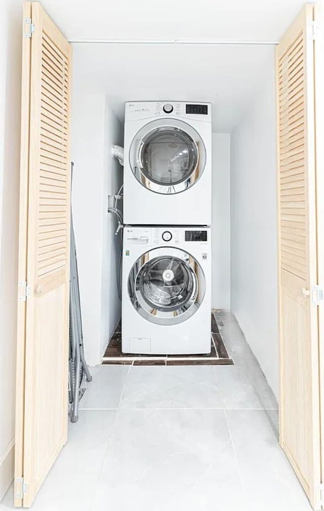 laundry area featuring light tile patterned floors, stacked washer / dryer, and laundry area