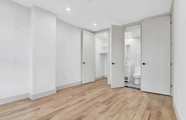 unfurnished bedroom featuring baseboards, recessed lighting, ensuite bathroom, a walk in closet, and light wood-type flooring