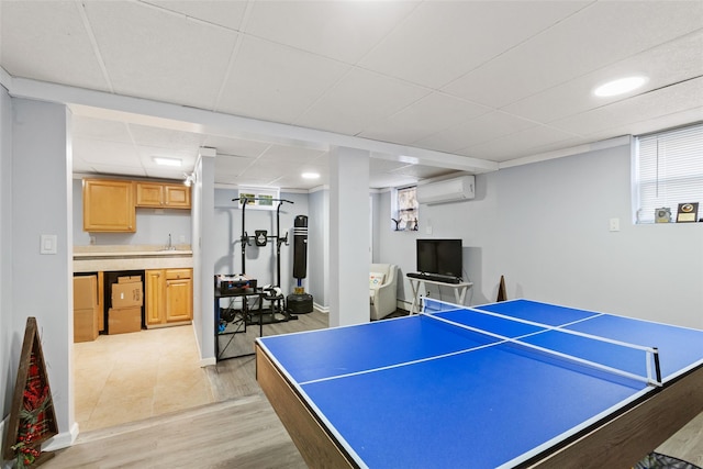 recreation room featuring a wall unit AC, light wood-style flooring, a paneled ceiling, and a sink