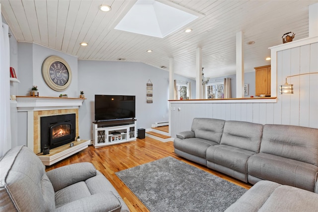 living area with lofted ceiling with skylight, a baseboard heating unit, wood finished floors, wooden ceiling, and a tile fireplace