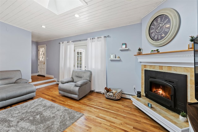 living room featuring wood finished floors, a skylight, a tile fireplace, a baseboard heating unit, and wooden ceiling