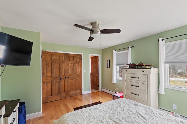 bedroom featuring a baseboard heating unit, baseboards, light wood-type flooring, and baseboard heating