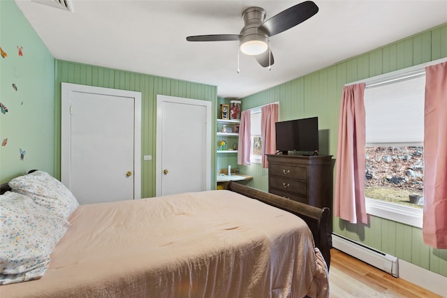 bedroom featuring multiple windows, wood finished floors, ceiling fan, and a baseboard radiator