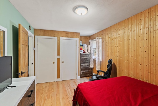 bedroom with multiple closets, light wood-style flooring, and wood walls