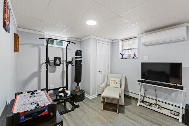 exercise room with baseboard heating, a paneled ceiling, a wall unit AC, and wood finished floors