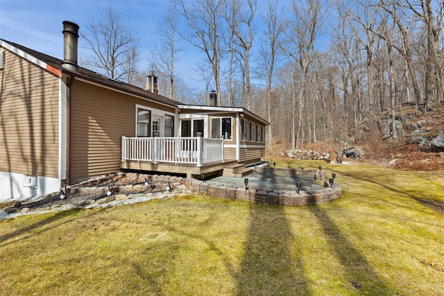 rear view of property featuring a wooden deck, a patio, a lawn, and a sunroom