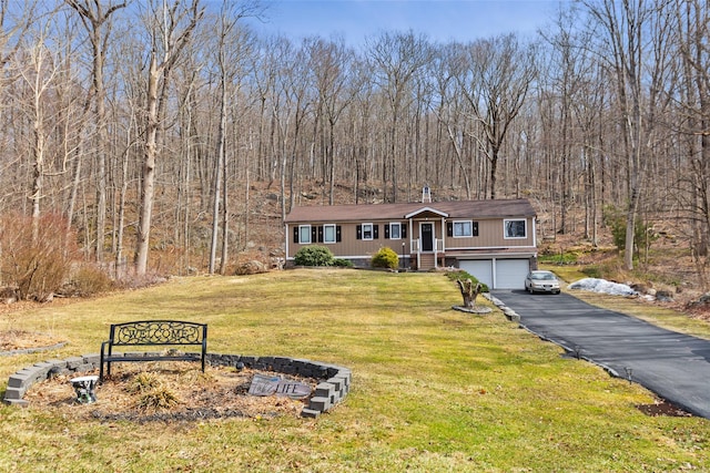 view of front of property with a front yard, an attached garage, a wooded view, and aphalt driveway