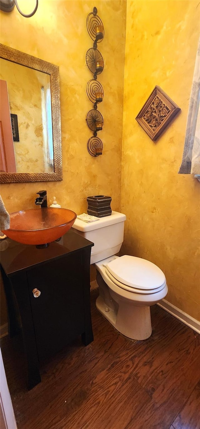 half bathroom with toilet, vanity, wood finished floors, and baseboards