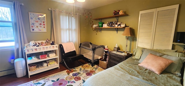 bedroom featuring a baseboard radiator, multiple windows, and wood finished floors