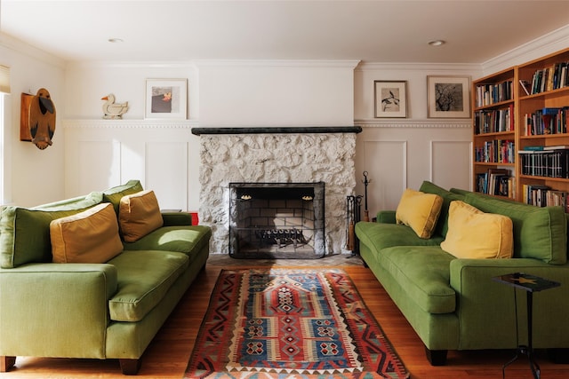 living area featuring a stone fireplace, wood finished floors, crown molding, and a decorative wall