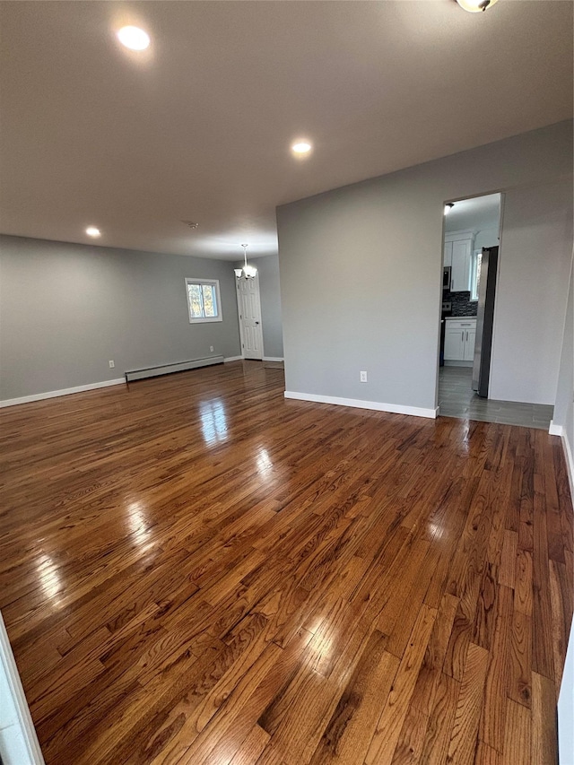 unfurnished living room featuring a chandelier, baseboards, a baseboard heating unit, and dark wood-type flooring