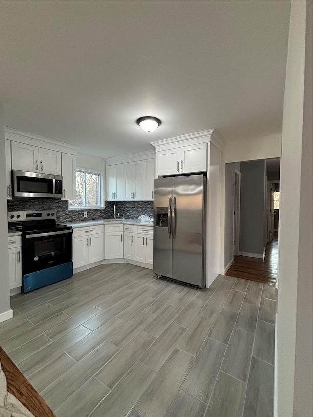 kitchen featuring wood finish floors, stainless steel appliances, decorative backsplash, and white cabinetry