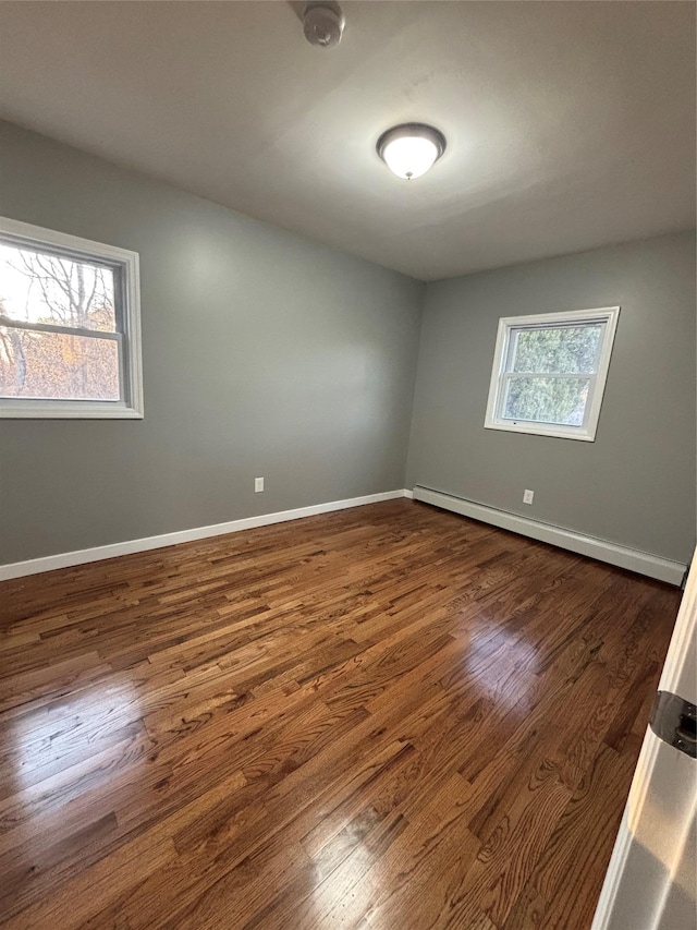 spare room with a baseboard heating unit, dark wood-type flooring, and baseboards