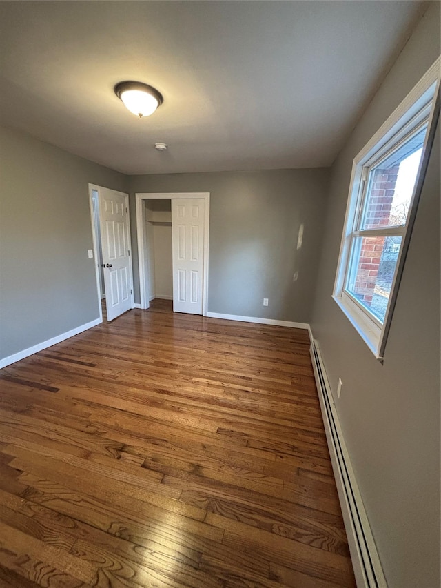 unfurnished bedroom featuring a baseboard radiator, baseboards, a closet, and dark wood-style floors