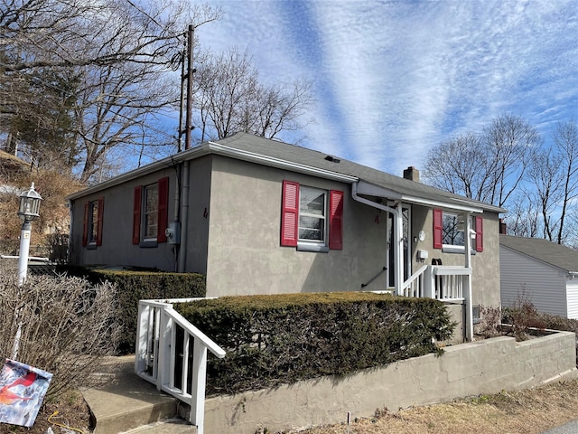 ranch-style house with stucco siding, roof with shingles, and a chimney