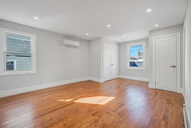 spare room with a baseboard heating unit, baseboards, an AC wall unit, hardwood / wood-style floors, and recessed lighting