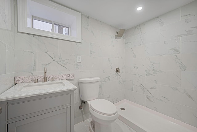 full bathroom with tiled shower, toilet, vanity, and tile walls