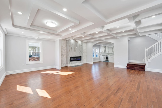 unfurnished living room with baseboards, stairway, a fireplace, coffered ceiling, and wood-type flooring