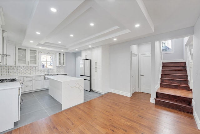 kitchen with light wood finished floors, backsplash, a center island, a tray ceiling, and freestanding refrigerator