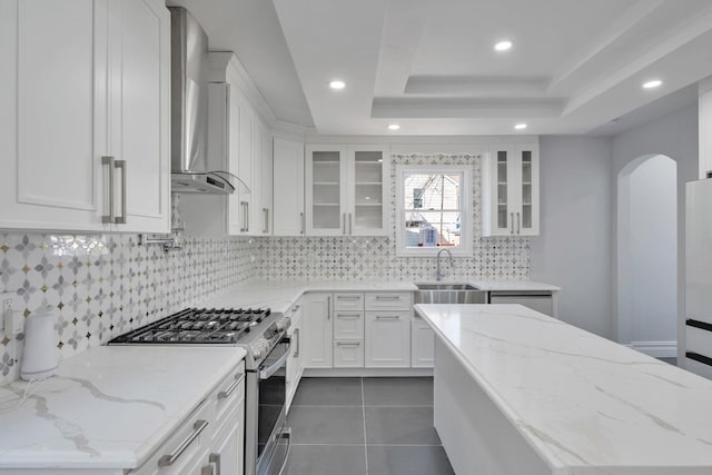 kitchen featuring a tray ceiling, wall chimney range hood, white cabinets, and stainless steel range with gas cooktop