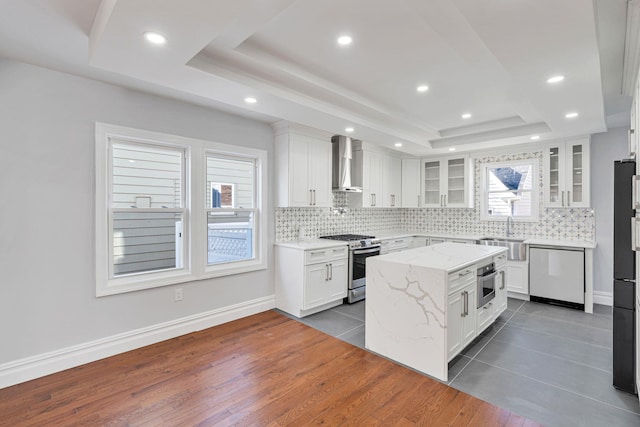 kitchen featuring stainless steel appliances, decorative backsplash, glass insert cabinets, a raised ceiling, and wall chimney range hood