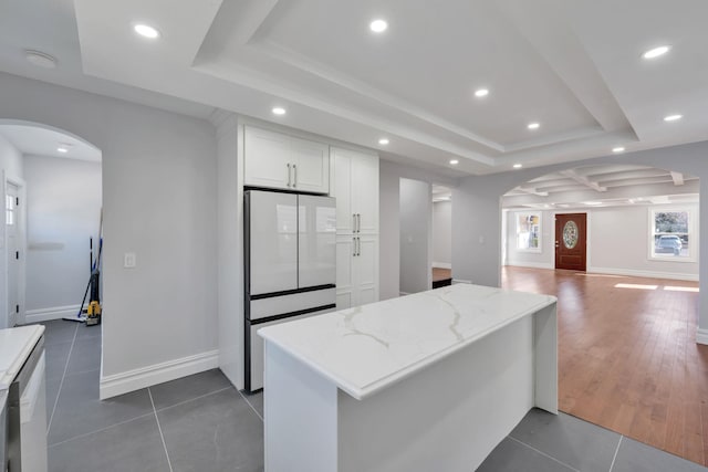 kitchen featuring dark tile patterned flooring, light stone counters, a tray ceiling, white cabinetry, and arched walkways