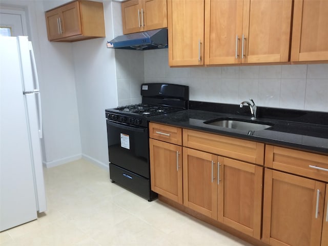 kitchen featuring under cabinet range hood, a sink, dark stone countertops, black gas stove, and freestanding refrigerator