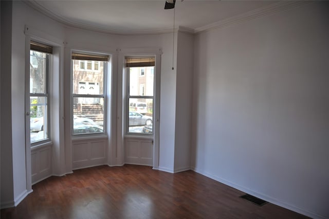 empty room featuring dark wood finished floors, visible vents, plenty of natural light, and ornamental molding