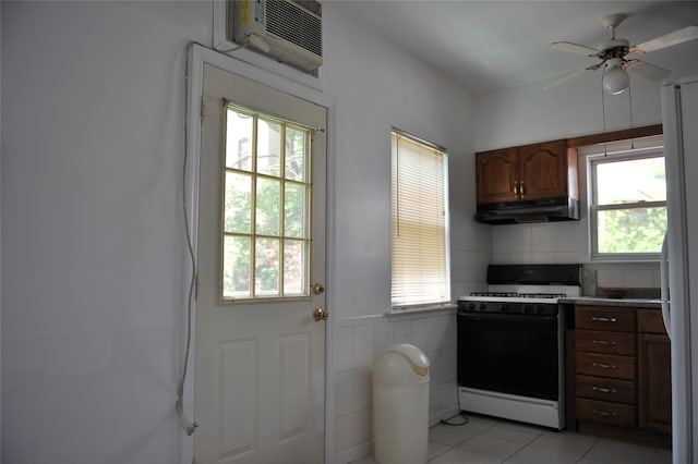 kitchen featuring under cabinet range hood, a wall unit AC, light tile patterned floors, gas stove, and a ceiling fan