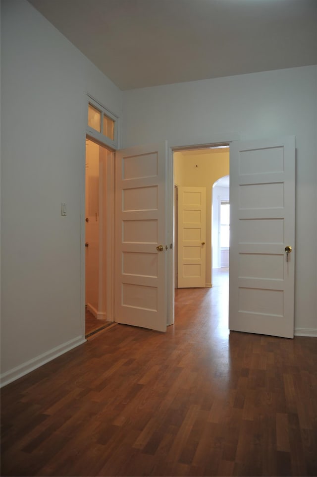 empty room featuring baseboards, arched walkways, and dark wood finished floors