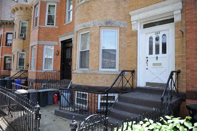 property entrance featuring cooling unit, brick siding, and fence